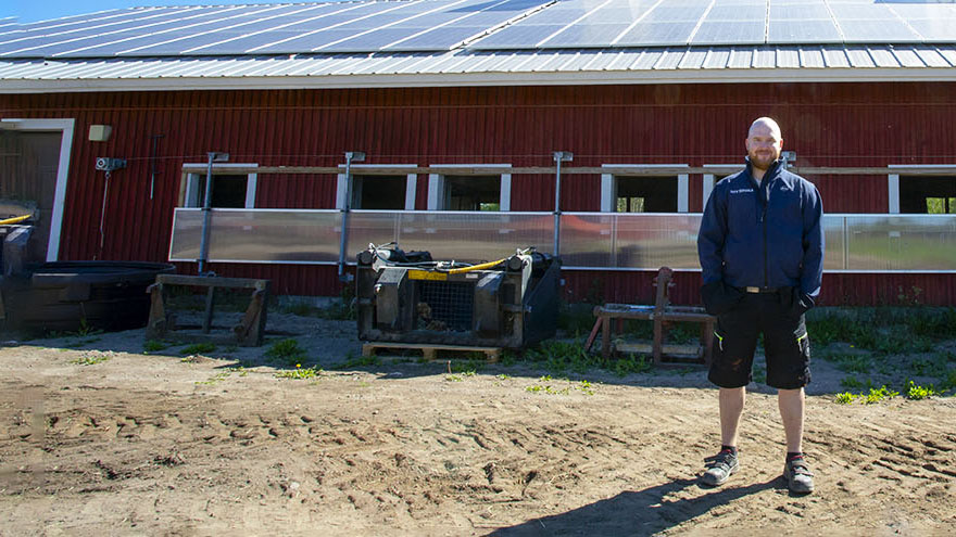 Tervalan lypsykarjatilalle asennetut aurinkopaneelit ja Eero Tervala seisoo rakennuksen edessä