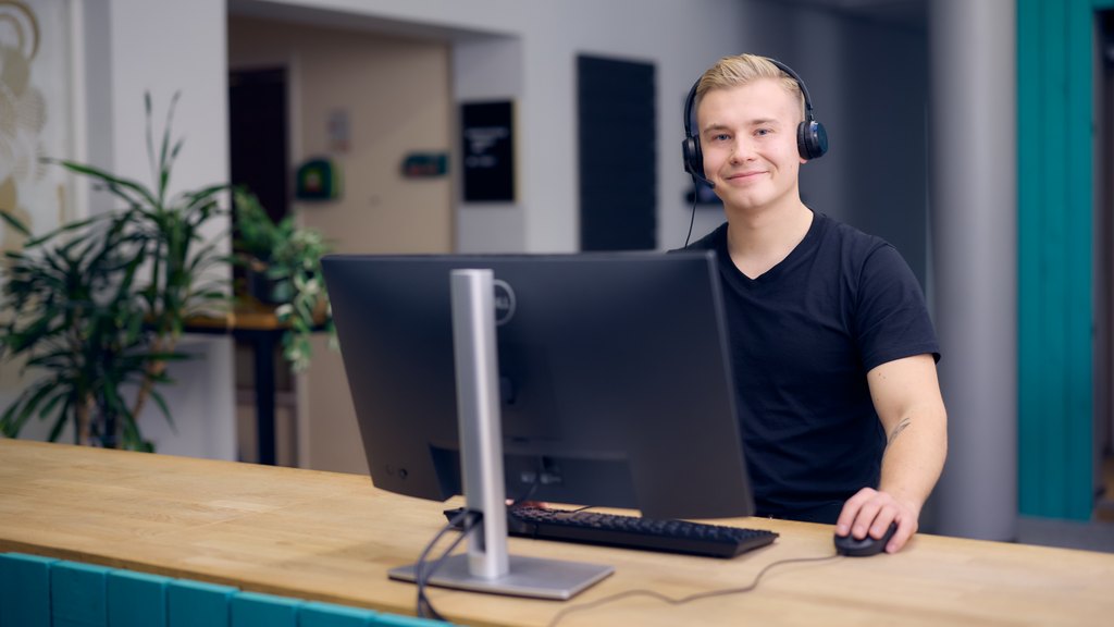 Kuvassa nivoslainen, joka tetee töitä tietokoneen äärellä kuulokkeet päässään.